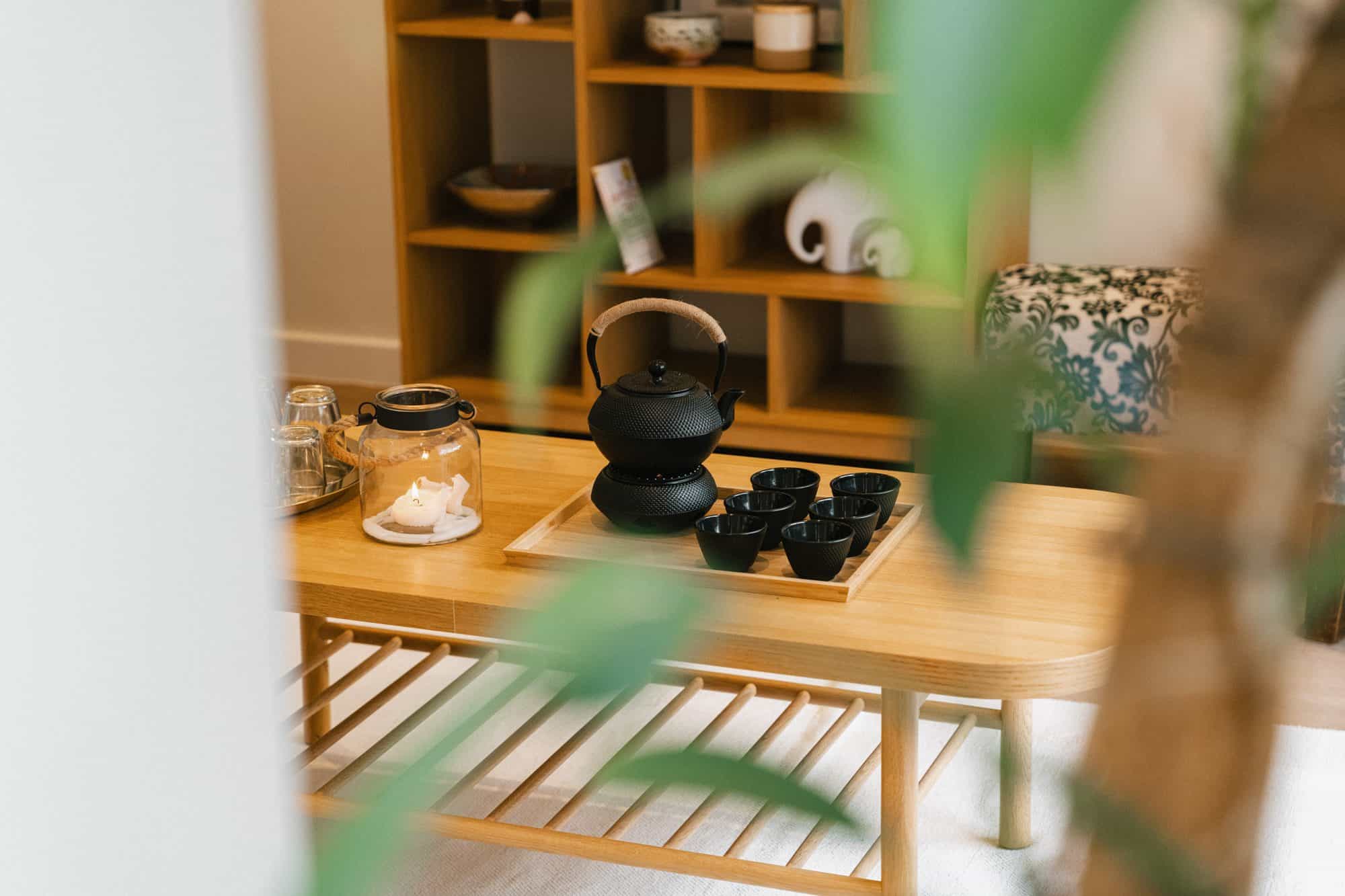 Cast iron teapot and cups on a timber table in the studio waiting area, framed by greenery